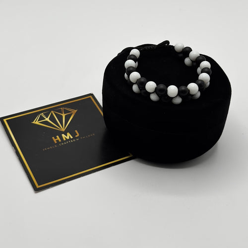 Black beaded bracelet on a black cushion with an HMJ card on a white background