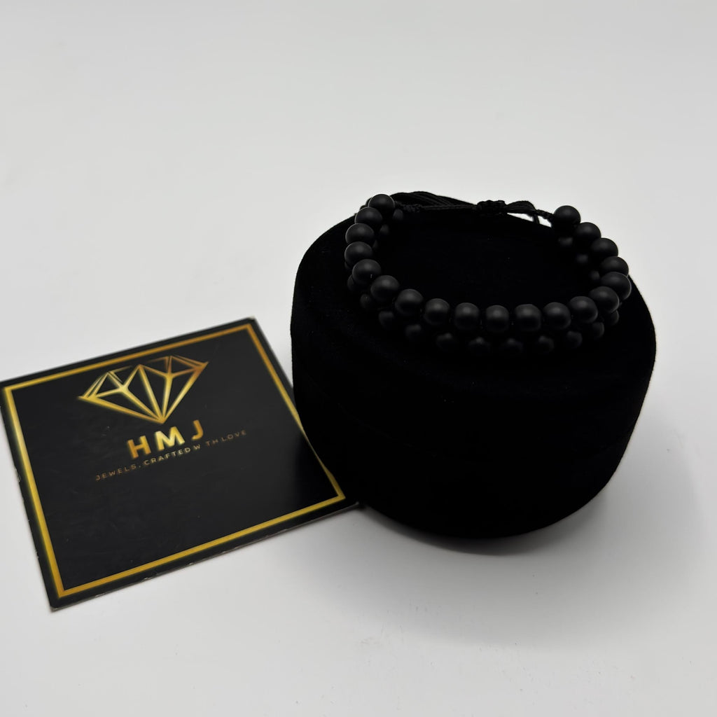 Black beaded bracelet in a black velvet bag with a gold and black card on a white background