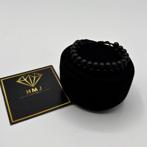Black beaded bracelet in a black velvet bag with a gold and black card on a white background