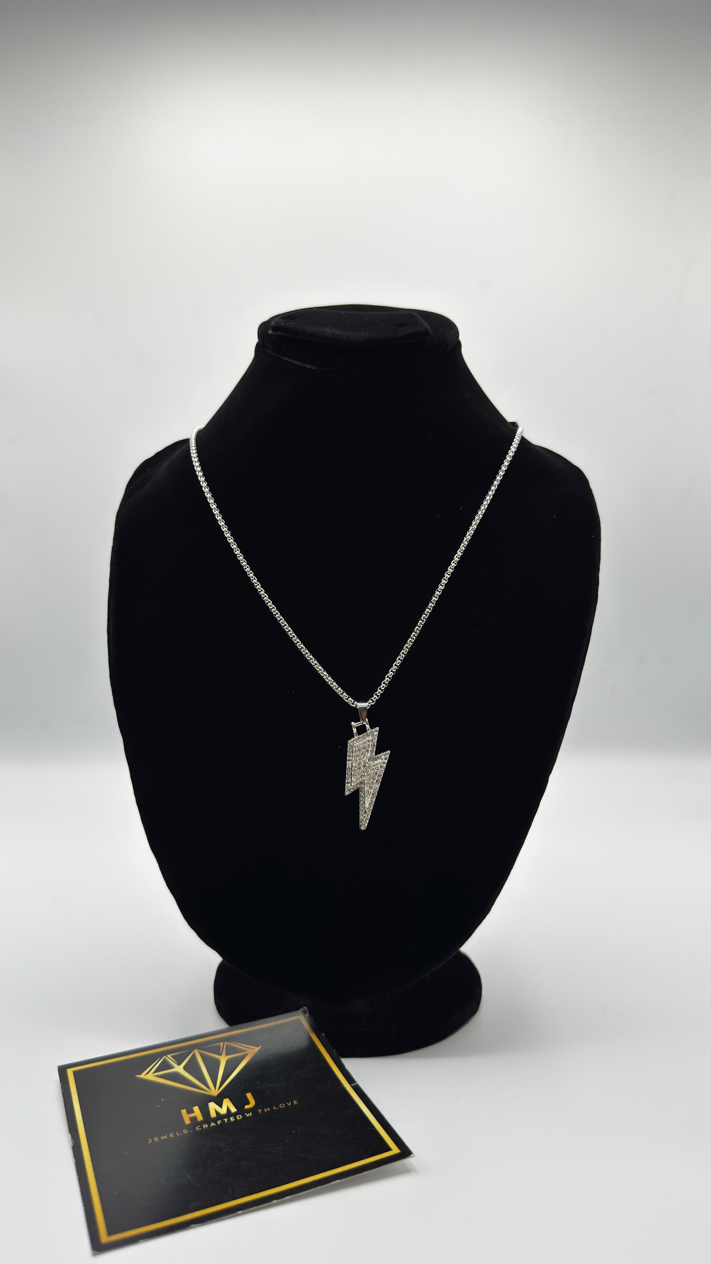 Necklace with a lightning bolt pendant on a black bust, accompanied by a branded card.