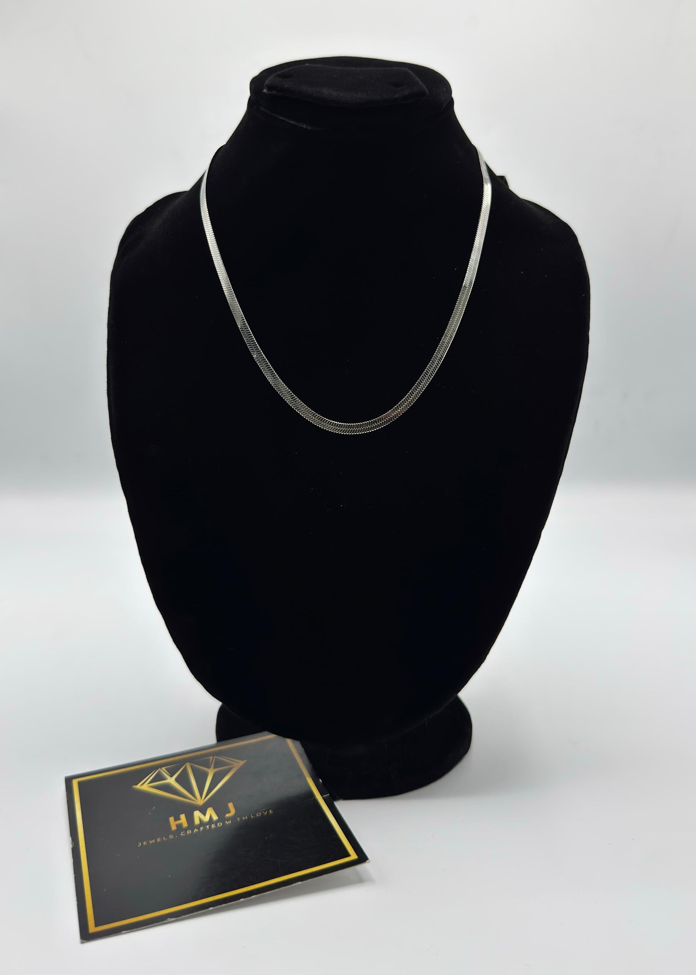 Black mannequin head with silver necklace and branded card on a white background